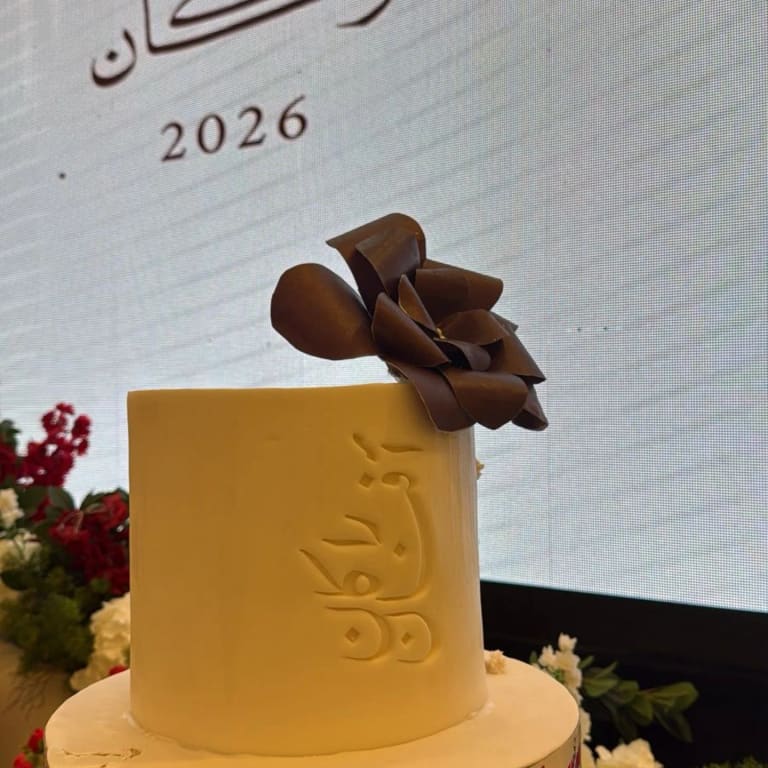 كيكة مربعة بلون الخردل عليها اسم منحوت بالخط العربي ووردة من الشوكولاتة